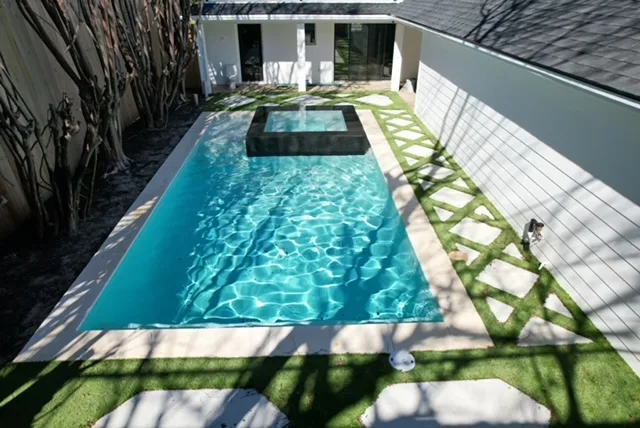Modern pool with dark spa and turf accents aerial view